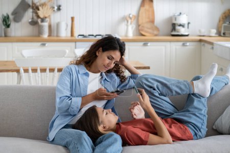 Photo for Young modern family mother and teen daughter busy with gadgets resting at home, mom and child using mobile devices while relaxing in living room on couch. Parent and kid spending time online - Royalty Free Image