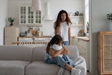 Photo for Strict mother scolding unhappy teenage daughter at home, mom lecturing teen girl, child sitting on sofa feeling afraid covering ears with hands. Parental harsh discipline, adolescent problem behavior - Royalty Free Image