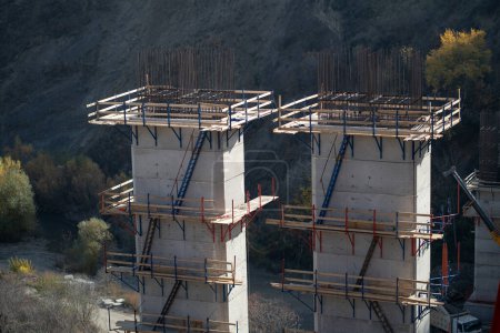 Photo for Supports of bridge under construction with wooden scaffolding and ladders for builders. Process of building transport infrastructure for railways or highways in difficult-to-reach mountainous areas - Royalty Free Image