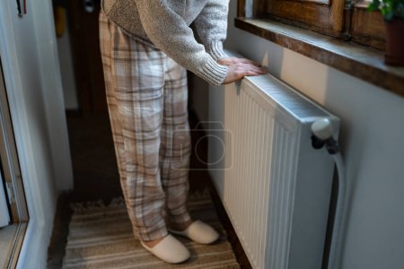 Photo for Closeup of woman warming her hands on the heater at home during cold winter days. Female getting warm up her arms over radiator. Concept of heating season, cold weather. - Royalty Free Image