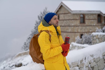 Photo for Thoughtful man walks with hot drink in thermal bottle thinks question, dreaming of future at winter frosty day. Relaxed male stands snow outdoor in yellow clothes for cold weather looks into distance - Royalty Free Image
