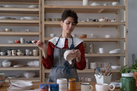 Photo for Concentrated young woman professional pottery artisan work in studio. Small business owner, teacher of ceramics preparing clay potter kitchenware for classes or selling in handmade handicraft shop - Royalty Free Image