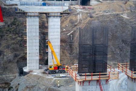 Téléchargez les photos : Process construction bridge for cars and road transport infrastructure in mountainous area. Two concrete piers for bridge with wooden scaffolding and metal frame are located next to cliff. - en image libre de droit