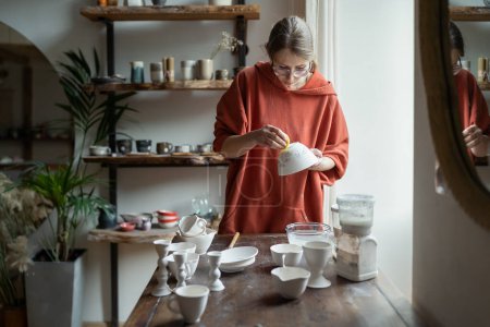 Photo for Creative young woman shaping clay bowl in studio. Concentrated female artist work on pottery in workshop space. Handicraft process for potter ceramic. Handmade hobby and sculpting concept - Royalty Free Image