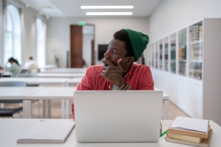 Photo for Procrastination concept. Thoughtful Black student man looking away while studying in library, pensive lost in thoughts African American guy learner disinterested in study looking into distance - Royalty Free Image