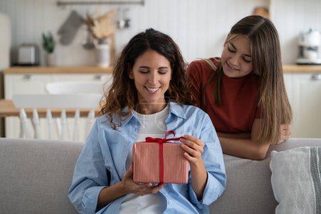 Photo for Happy mothers day. Teen girl daughter making surprise for mom, congratulating mother with birthday at home. Happy excited young woman getting wrapped gift box present from child while sitting on sofa - Royalty Free Image