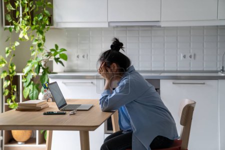 Foto de Unhappy frustrated young woman sitting at kitchen table looking at laptop screen having problems in job searching, reading bad news via email. Upset student girl feeling unmotivated to study online - Imagen libre de derechos