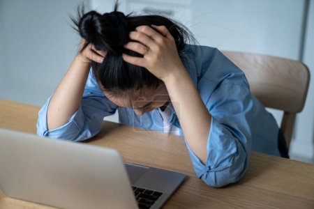 Téléchargez les photos : Stressé frustré jeune femme e-commerce entrepreneur assis au bureau avec ordinateur portable tenant la tête dans les mains, ayant des problèmes d'affaires en ligne, accent sélectif. Travail indépendant et santé mentale - en image libre de droit