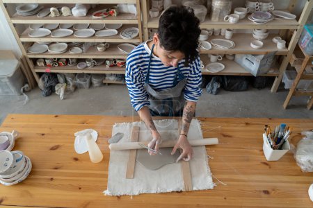 Téléchargez les photos : Jeune femme potier travail avec de l'argile sur table de poterie dans l'espace d'art créatif, studio professionnel. Artiste féminine créant de la céramique artisanale pour passe-temps. Détendez-vous au concept d'atelier de produits artisanaux - en image libre de droit