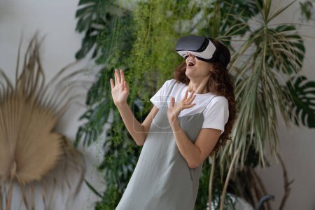 Téléchargez les photos : Jeune femme ravie de passer du temps libre dans la réalité virtuelle tout en se relaxant dans le jardin à la maison, jardinière stupéfaite jouant à des jeux VR, en utilisant la technologie interactive. Concept de cyberespace. - en image libre de droit