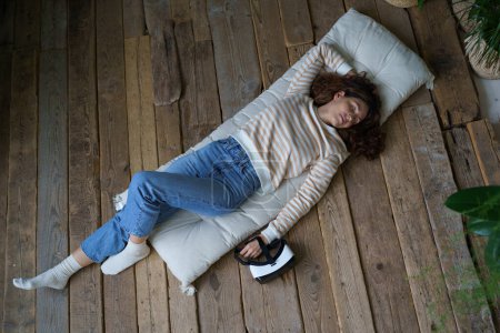 Photo for Relax woman in jeans with virtual reality glasses sleeping on wooden floor at home. Calm young female lying down on comfortable mattress taking a nap for wellness and health after a long day - Royalty Free Image