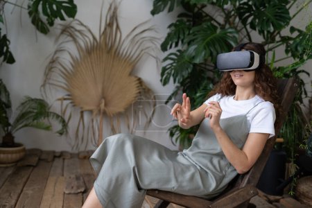 Photo for Excited italian woman leaning on chair, resting, wearing vr headset, raising hands touching air with fingers while playing in virtual games in home garden. Cyberspace concept. - Royalty Free Image