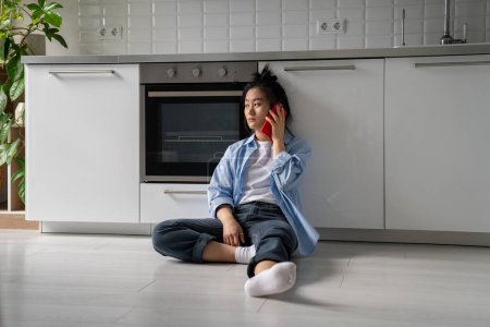 Photo for Unhappy worried Asian young woman feeling depressed thinking of personal problems looking to side trying to call psychotherapist by cellphone from home. Miserable girl suffering relationship troubles. - Royalty Free Image