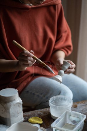 Photo for Process of making clay products using brush and water to smooth out irregularities. Craft master holding in hand piece earthenware prepare for drawing glazing and firing in ceramic kiln in workshop. - Royalty Free Image