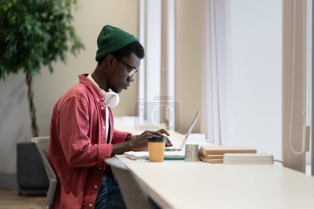 Photo for Thoughtful man freelancer typing on laptop keyboard send email write message for project at workplace. Serious pondering African American hipster male using internet banking service search information - Royalty Free Image
