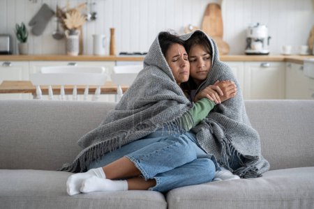 Photo for Oppressed unhappy family mother and teenage girl are trying to keep warm wrapped in warm blanket sits on couch. Weakened suffering woman with teenage daughter suffers after breakdown heating equipment - Royalty Free Image