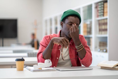 Photo for Tired student think about trouble rubs bridge of nose while take off glasses. Frustrated African American man can not concentrate on study due to pain in eyes. Nervous breakdown or emotional crisis. - Royalty Free Image