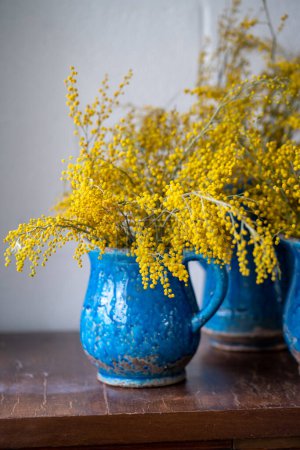 Téléchargez les photos : Bouquet de fleur de Mimosa en vase en céramique vintage bleu se tenir sur le mur blanc à la maison. Bouquet de printemps avec Acacia dealbata sur surface en bois, mise au point douce. 8 mars, concept de Pâques - en image libre de droit