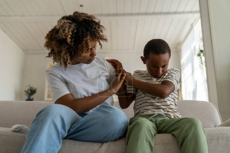 Photo for Angry offended child african american boy ignoring mother, upset mom parent trying to embrace stubborn son while sitting together on sofa at home. Parenting adopted children with challenging behavior - Royalty Free Image