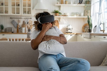 Foto de Asustado sorprendido mujer afroamericana en gafas 3d viendo horror vídeo VR mientras se relaja y pasar el tiempo libre en casa, sentado en el sofá, emocionado chica negra asombrada en equipo de realidad virtual - Imagen libre de derechos