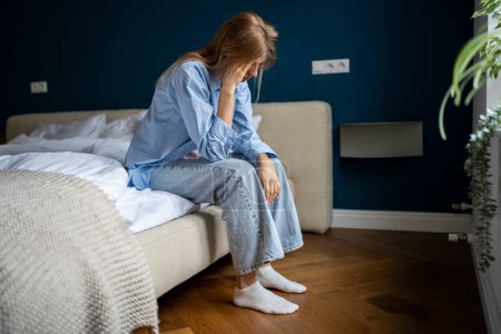 Photo for Loneliness and mental health. Depressed unhappy young woman sitting on bed at home suffering from depression, having melancholy mood. Caucasian female feeling unwell, having headache - Royalty Free Image