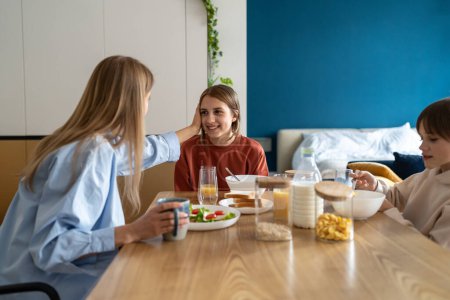 Photo for Happy caucasian family single mother and two kids enjoy healthy breakfast, spending time at home together, loving mom communicating talking with children while sitting at kitchen table in morning - Royalty Free Image