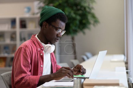 Photo for Involved in remote job African American hipster man freelancer using laptop computer while sits at modern coworking, types message email writes publication for web creates new project investment plan. - Royalty Free Image
