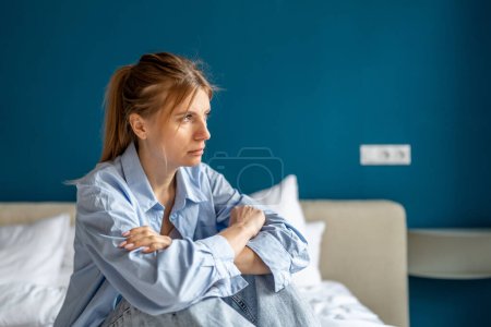 Téléchargez les photos : Stressé nerveux bouleversé femme assise sur le lit regard dévasté dans la distance perdue dans les pensées. Déprimé femme inquiète souffrent d'apathie, épuisement émotionnel, ayant des problèmes personnels, besoin d'aide psychologique - en image libre de droit