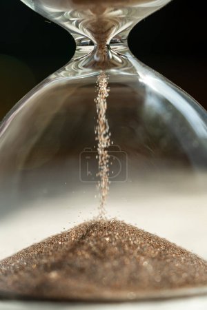 Photo for Shiny sand running in inverted hourglass lasting certain amount of time as transience of life. Accessory for home measuring passing time to deadline. Small grains of sand fall into hole of glass flask - Royalty Free Image
