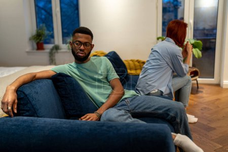 Photo for Unhappy young interracial couple sit separately on sofa at home, tired of each other, upset family man and woman not talking after fight, sit on couch apart. Bad communication in relationship - Royalty Free Image