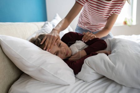 Photo for Sick little boy lying in bed, having chills and fever. Mother checking childs temperature touching forehead of unhealthy schoolboy son. Kid with respiratory illness symptoms. Childcare and influenza - Royalty Free Image