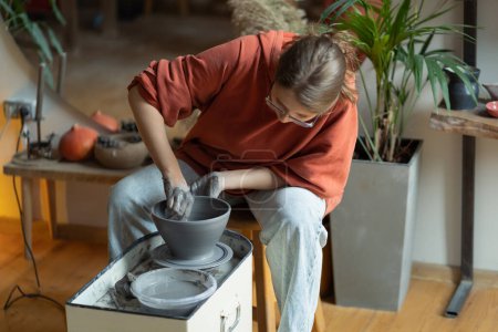 Photo for Creative focused woman learning sculpting working with potter wheel on making bowl for future artworks. Carried away young girl sits in homemade craft workshop wishing to become professional sculptor - Royalty Free Image