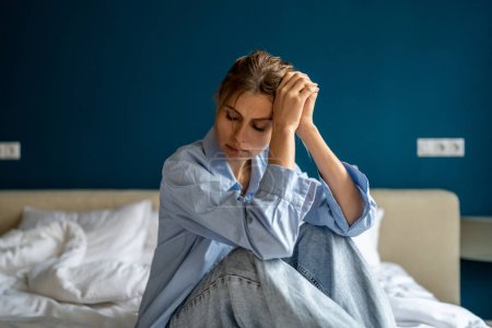 Photo for Young unhappy woman sitting on bed at home, waking up depressed, suffering from depression, feeling sad and miserable. Female suffering from post-traumatic stress disorder. Women and mental health - Royalty Free Image