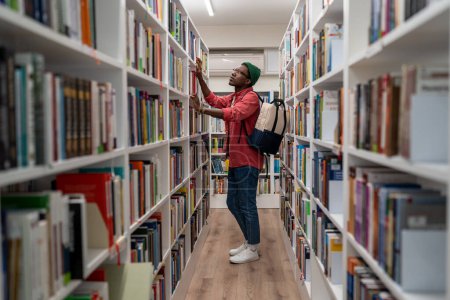 Photo for Thoughtful Black student guy searching materials for educational research in college library. Young African man choosing book for reading in bookstore, selective focus. Literature and education - Royalty Free Image