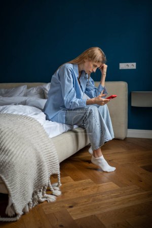 Photo for Worried tired woman bowing head sadly looking at screen smartphone waiting call feeling unwell need psychological help. Depressed young female hold mobile phone suffering headache from divorce stress - Royalty Free Image