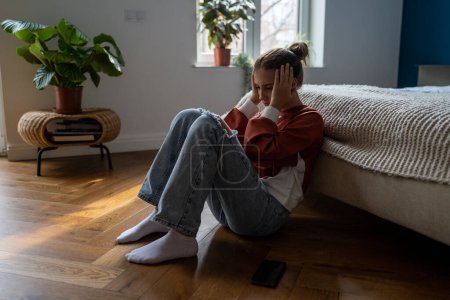 Photo for Frustrated sad teen girl child sitting alone on floor being bullied online, having feelings of isolation and fear. Depressed teenage kid holding head in hands dealing with first love heartbreak - Royalty Free Image