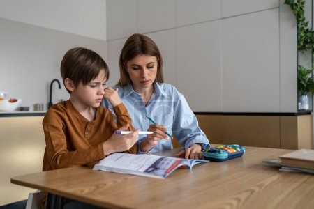 Photo for Caucasian mother and schoolboy son preparing school homework together at home, mom homeschooling parent helping little boy child with home task, sitting at kitchen table. Children and education - Royalty Free Image