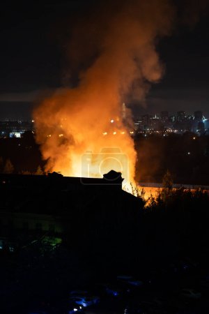 Photo for Building on fire at night in city. Orange flames and heavy smoke pouring out of burning damaged house during nighttime. Fire hazard in buildings concept - Royalty Free Image