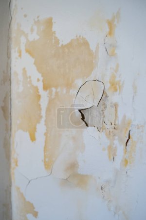 Photo for Damaged wall with chipped paint and plaster in traces of leak from faulty water supply at neighbours. Yellow rusty spots from dampness and mold in unheated room. Leaky roof dampness in bedroom ceiling - Royalty Free Image