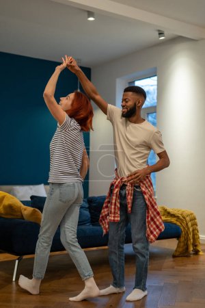 Photo for Happy loving young diverse couple dancing romantic dance in modern bedroom with panoramic windows. Smiling husband and wife celebrating anniversary, enjoying tender moment, having fun at home. - Royalty Free Image