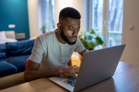 Photo for Focused African American guy freelancer using laptop at home, overworked black man working on project all night at home office, student guy remote studying looks at computer screen feeling tired - Royalty Free Image