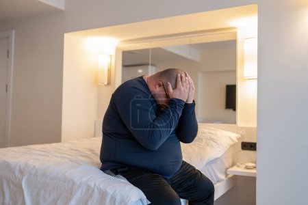 Photo for Frustrated confused depressed man sitting in bed at home closing face with hands worrying about life troubles. Male feels disappointment having problems. Overweight bearded guy has midlife crisis. - Royalty Free Image