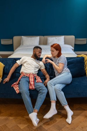 Photo for Conflicting multi ethnic stressed couple sitting on couch discussing at home. Man woman talking face to face trying come to agreement, understanding. Misunderstanding, relationship crisis, problems. - Royalty Free Image