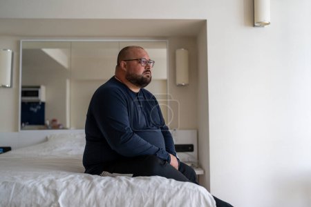 Photo for Frustrated overweight man sits on bed sadly looking to window feeling depression from difficult relations, works trouble, health problem. Unhappy male think about hopelessness need psychological help - Royalty Free Image
