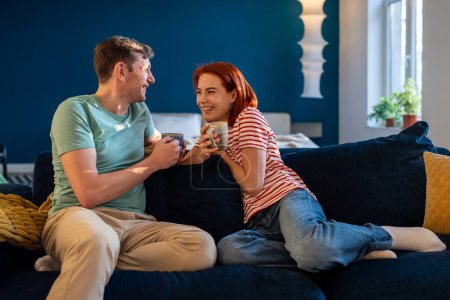 Foto de Joven pareja familiar romántica feliz hablando y sonriendo, conociéndose mejor, bebiendo té, se sienta en el sofá en casa, pasando tiempo juntos. Comunicación en la relación, amor en el matrimonio - Imagen libre de derechos