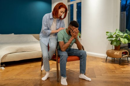 Photo for Unhappy diverse couple discussing divorce at home, husband feeling sad and frustrated after difficult conversation with wife. Loving girlfriend trying to comfort crying boyfriend embracing him - Royalty Free Image