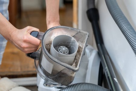 Photo for Woman opening dust filter out of vacuum cleaner at home. Hoover container full of dirt, fur, pet hair after cleaning at home. Housework, household chores. Dust in apartment is source of allergies. - Royalty Free Image