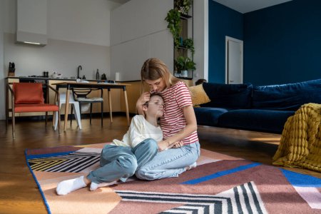 Photo for Mother-son bond. Young woman loving mother hugging boy son while relaxing together at home, sitting on floor. Mom parent cuddling child showing him affection. Single parenting concept - Royalty Free Image