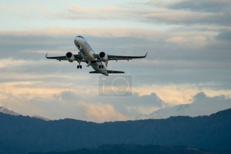Passenger airplane after takeoff against backdrop of mountains and sunset cloudy sky on background. Plane taking off from Batumi airport in Georgia. 