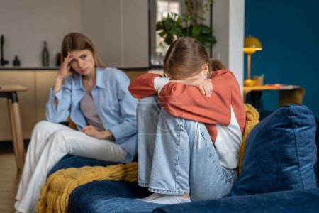 Photo for Upset worried mother looking at crying moody teenage daughter, sitting together on sofa, upset frustrated mom and teen girl child not talking after argument, having communication problems - Royalty Free Image